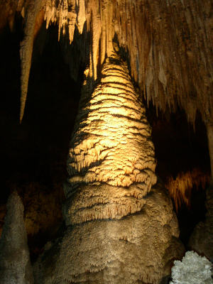 [A yellowish light shines not only on the stalagmite, but also on the many spear-like stalactites hanging from above. It also looks like portions of the rock are 'melting' off the stalagmite.]